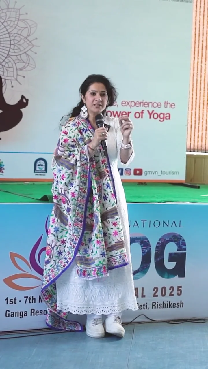 Charu Wadhwa speaking with a microphone on stage at the International Yog Festival 2025